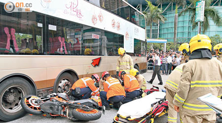 巴士玻璃被電單車撞爆（箭嘴示），救護員在場為鐵騎士急救。（梁卓明攝）