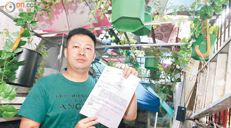 鍾俊輝在花架下展示司法覆核的文件。
