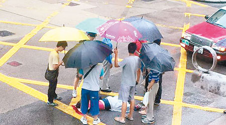 被撞傷女子倒臥地上，一批熱心途人為其擋雨。（網民Billy Wong攝）