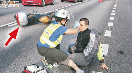 聖約翰救傷隊隊員為傷者急救，涉事電單車則橫亘路中（箭嘴示）。（梁卓明攝）