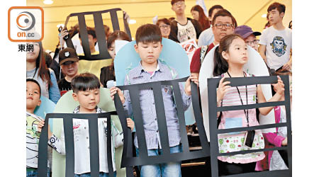 學童背上不同訴求的紙書包及舉起象徵困擾學童的「牢籠」遊行。（胡家豪攝）