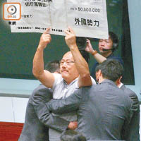答問大會開始後，陳偉業高舉巨型支票道具示威被逐。