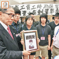社民連成員向梁智鴻遞上寫有「過勞死」字樣的相框令會議暫停十分鐘。