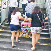 旺角<br>在旺角染布房街連接旺角東港鐵站的行人天橋，遊客林小姐與友人合力抬起逾十公斤的行李篋上橋。