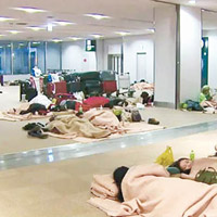 部分滯留旅客在機場客運大樓內席地而睡。（電視畫面）