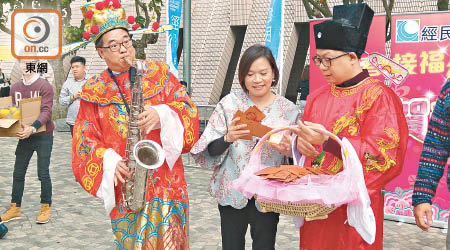 盧偉國（左）扮財神吹色士風同市民拜年，而梁美芬（中）就大派金幣利是。（陳宛彤攝）