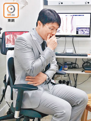 脊醫王俊華示範正確咳嗽姿勢：靠着椅背借力，左手輕抱腹肌，把咳嗽衝力從頸椎卸走。（張汶樂攝）