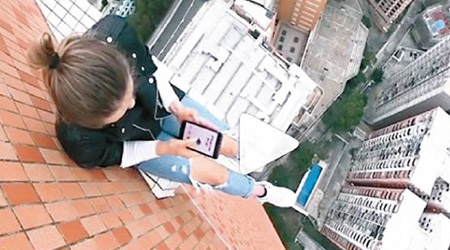 Angela Nikolau危坐橙磚建築物天台外牆的凸起小位置玩手機遊戲。（互聯網圖片）