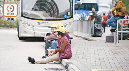 旅客坐在巴士站路邊。（黃偉邦攝）
