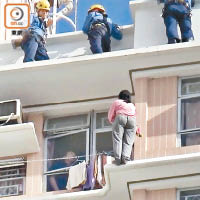 抱着嬰兒的婦人危站簷篷，消防員在樓上戒備。