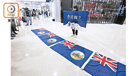 黑衣人展示港獨旗，又將港英旗鋪在地面。（何天成攝）