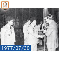 當年駐港三軍司令夏卓賢爵士（右）授旗予香港童軍慶祝英女王登基銀禧紀念出訪星、馬、泰及印尼等國的名譽領隊馬惜珍先生（前中）。