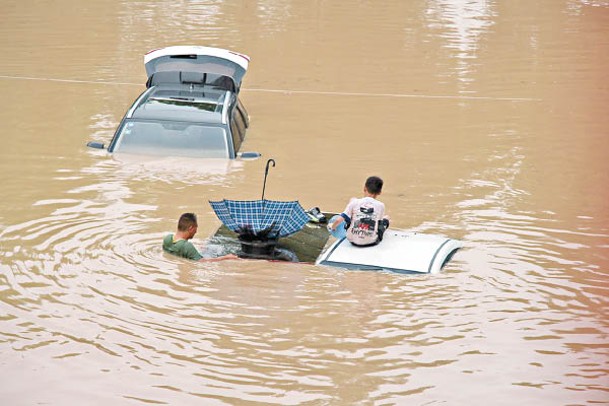 車輛近乎滅頂，民眾坐在車頂上等候救援。