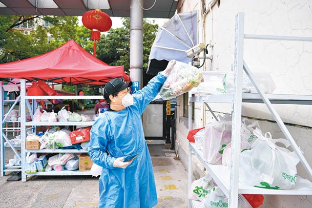 上海市封控區配送員把蔬菜包放在貨架。（中新社圖片）