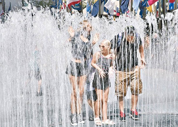 紐約市民在噴水池戲水降溫。（中新社圖片）
