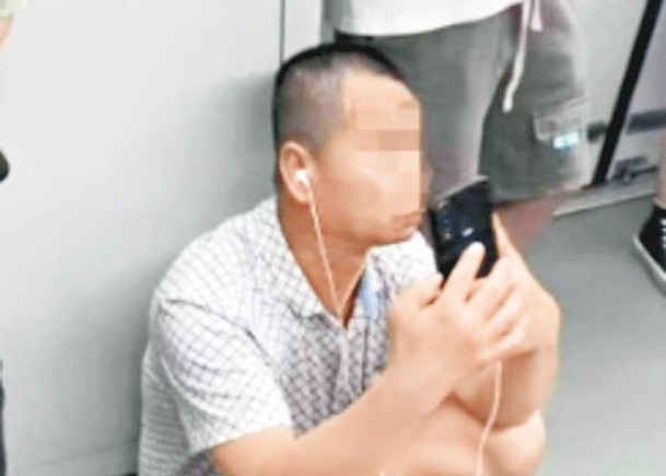 男事主蹲在地鐵車廂地板上玩手機。