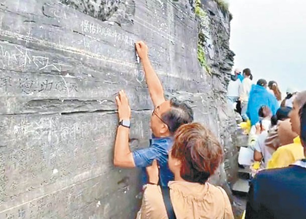 男子和一名婦人在崖壁上以疑似鑰匙的物體肆意刻字。