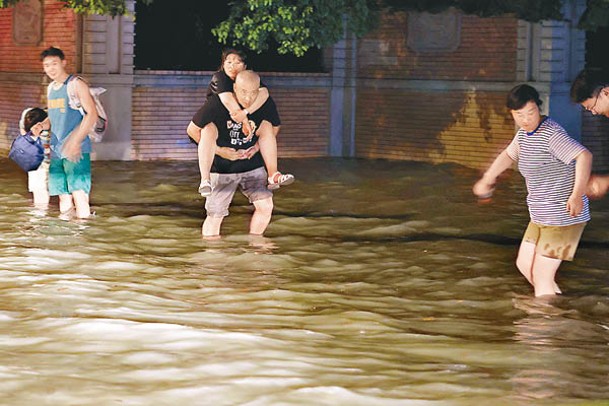 上海市閔行區居民背着家人在水中行走。（中新社圖片）