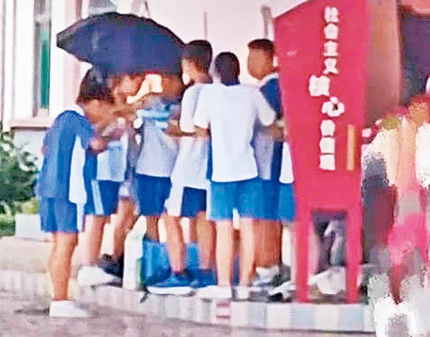 身穿校服的男女學生聚在一起，在校園一角站着吃飯。