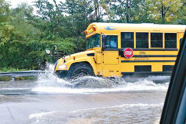 紐約有校車駛過積水的路段送學童上學。