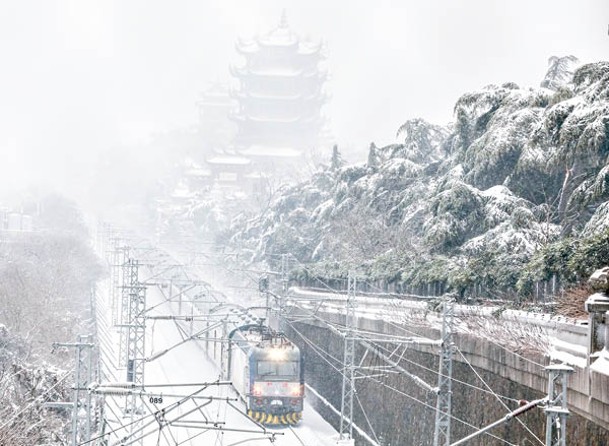 湖北：列車在雪中駛過武漢黃鶴樓。（中新社圖片）