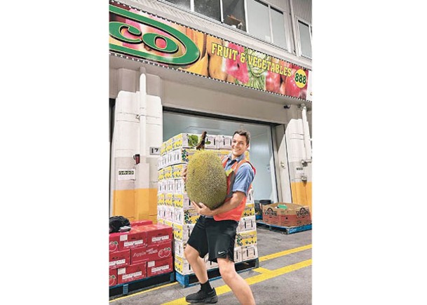 一名市場員工用雙手抱起大樹菠蘿。