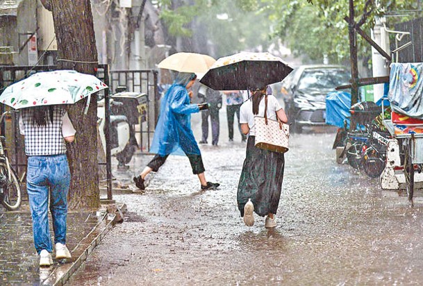 北京市發布暴雨黃色預警，市民涉水走過小巷。