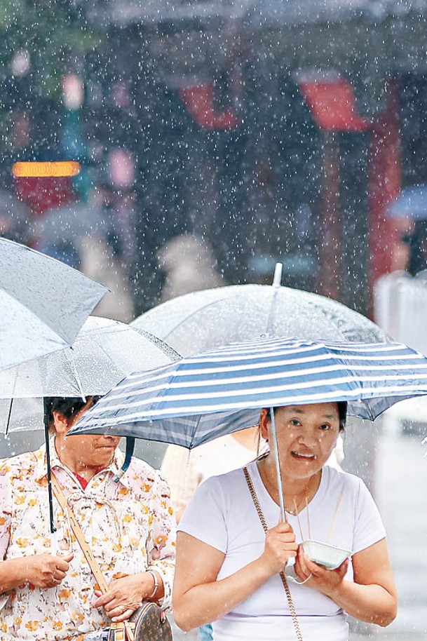 南京市民撐傘在雨中出行。