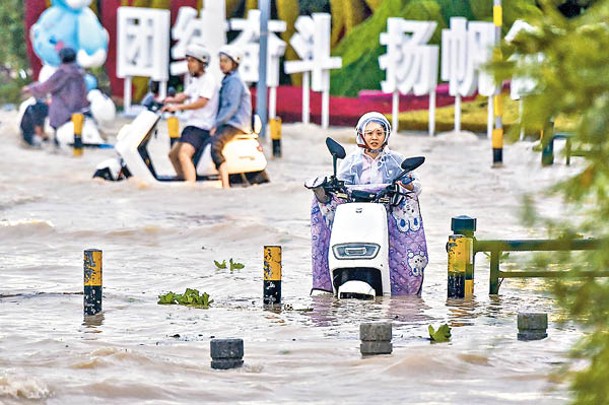 三亞市鹿城大道積水嚴重，民眾騎電動車通過積水路段。（中新社圖片）