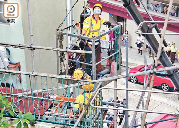 大型工程車輛將工人吊至鄰近大廈外牆進行拆棚架工程。（蘇偉明攝）