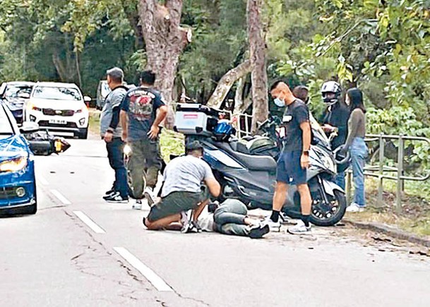 新娘潭路﹕事主倒臥路面，車友陪伴在側。