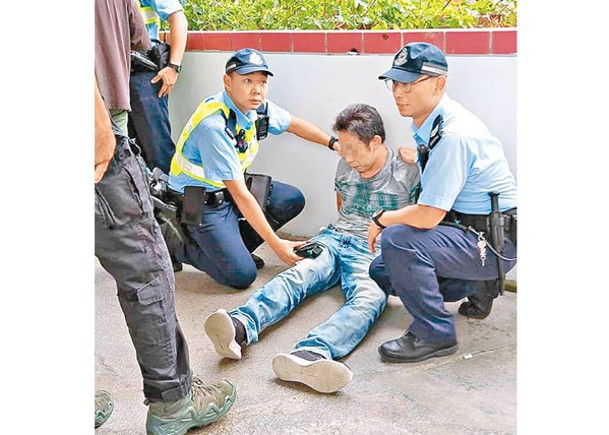 被捕男子坐在地上，由執法人員看管。