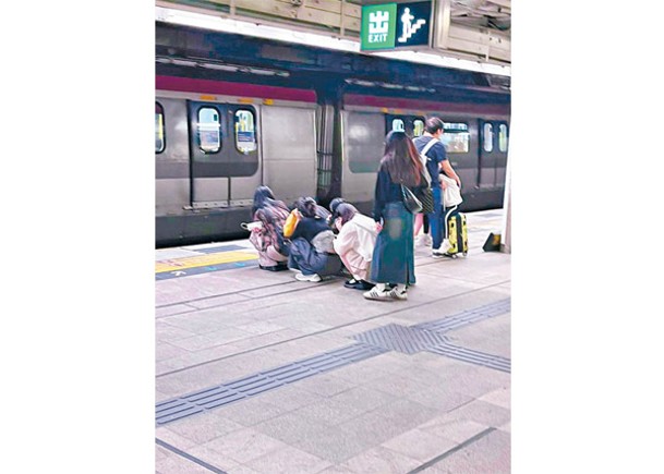 數名少女蹲在月台黃線位置等車。