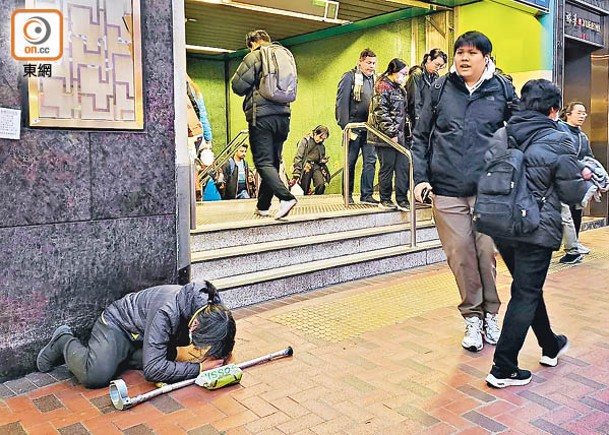 持拐杖男子以跪拜的方式在港鐵站出口，向行人乞討金錢。（劉子文攝）