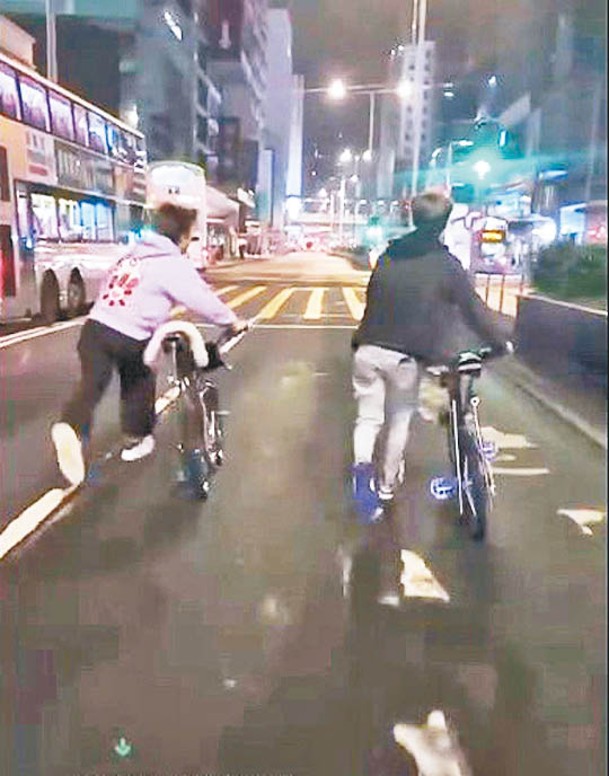 兩名年輕人推着單車在馬路上賽跑。