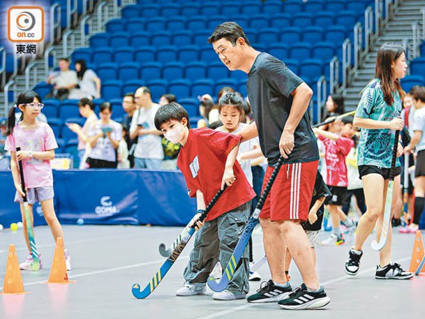 專業教練指導小朋友打曲棍球。