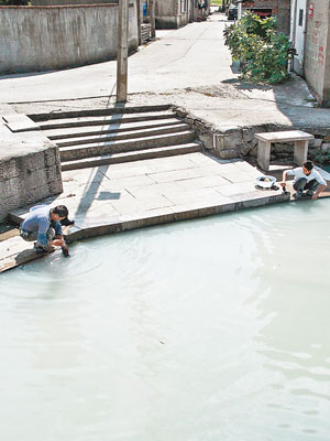 兩名村民仍用乳白色的河水洗滌衣物。（中新社圖片）