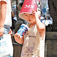重慶<BR>重慶街頭有小孩以快餐盒當太陽帽，一手拿着凍飲解暑。（中新社圖片）