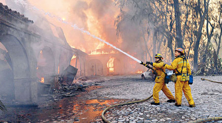 山火波及民居，消防員灑水灌救。
