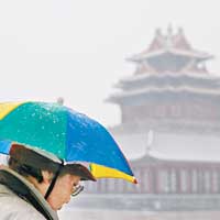 北京<br>北京迎來初雪，一名街上途人頭戴傘帽擋雪。（中新社圖片）