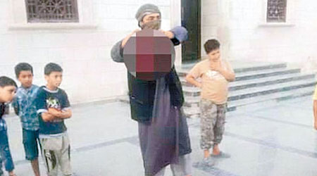 IS成員把俘虜斬頭後，將首級向數名小孩展示。（互聯網圖片）