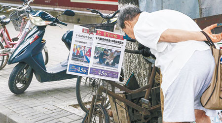 北京街頭有市民低頭關注報紙頭版有關令計劃被雙開的消息。（中新社圖片）