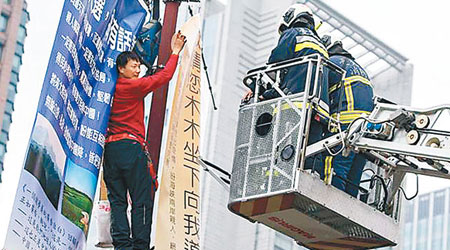 畢男爬上台北市府前廣場掛上三幅海報。（中時電子報圖片）