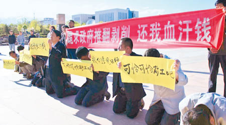 該礦區的欠薪員工代表跪在政府前，高舉橫額示威。（互聯網圖片）
