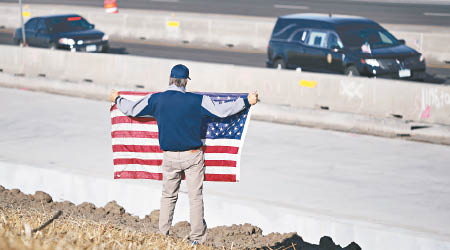 載有帕里什遺體的汽車經過時，有市民舉起美國旗致敬。（美聯社圖片）