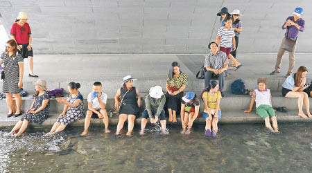 首爾受熱浪侵襲，民眾在河邊浸腳乘涼。（美聯社圖片）