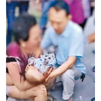 婦人手抱受傷嬰兒坐在路旁。