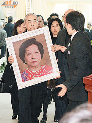 林建名捧着母親的遺照，神情哀傷。
