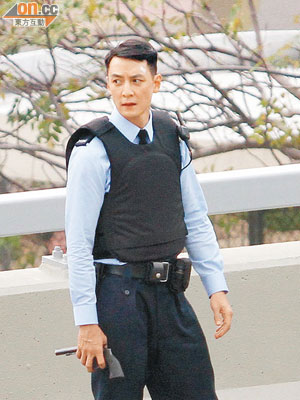 穿上避彈衣的吳彥祖型警look，手執槍準備拍攝。