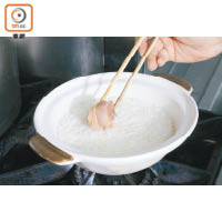 2. 洗米後加水浸約10分鐘，大火煲約10分鐘至沸騰後，轉中火放入冬菇、雞件和葱白，冚蓋煲約10至15分鐘。